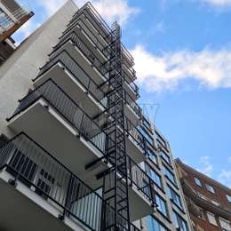 Escalera fija sin jaula integrada al frente de los balcones de un edificio de apartamentos.