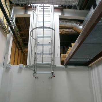 Drop-down ladder with a cage in an industrial environment.