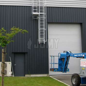 Drop-down ladder with double cage and resting platform outside of a warehouse.