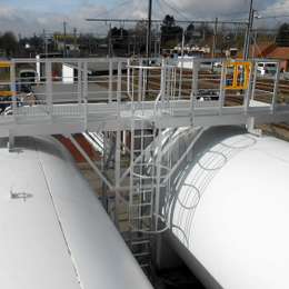 Échelle à crinoline utilisée pour accéder à une plate-forme industrielle sur deux réservoirs de stockage horizontaux.