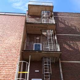 Escaleras con jaula para escape de incendios desde una ventana y balcones de acceso de hormigón.