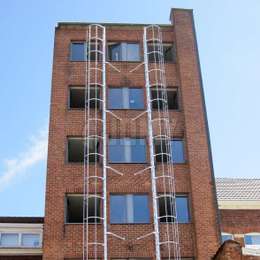 2 escaleras de jaula colocadas perpendiculares a la fachada, junto a las ventanas y utilizadas para la evacuación de un edificio de 7 pisos.