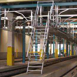 Escalera de mano industrial para acceso a plataforma con pasarela en un taller de mantenimiento de trenes.