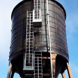 Escaleras fijas con línea de vida vertical y plataformas de apoyo sobre silo.