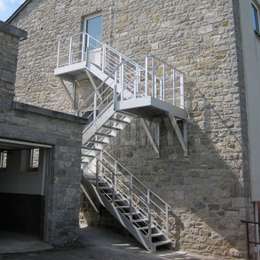 Escalera industrial suspendida en la fachada de un edificio de 2 pisos.