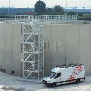 Escaleras de 3 pisos y plataforma industrial utilizada para acceder a un tanque de almacenamiento de concreto en una planta industrial.