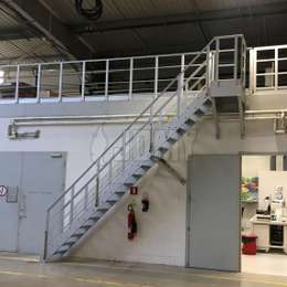Escalier d'accès pour une mezzanine industrielle, avec une rampe murale additionnelle.