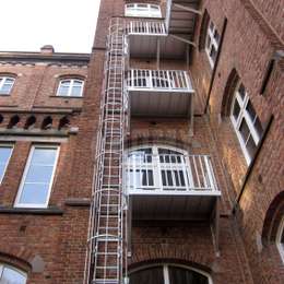 3-stöckige Käfig-Feuerleiter mit Zugangsbalkon auf jeder Ebene eines Fabrikgebäudes.