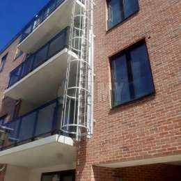 Drop-down ladder with cage for fire escape from the balconies of a modern apartment building.