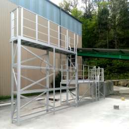 Fixed access platform with two levels, fixed ladders and guardrails, used for accessing truck trailers and loads.