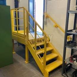 Painted industrial stairs and landing platform with wall handrail.