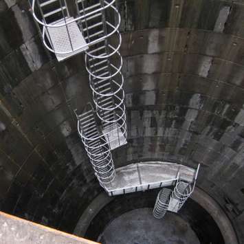 Käfigleiter mit Ruheplattformen in einem industriellen Reservoir/Brunnen.
