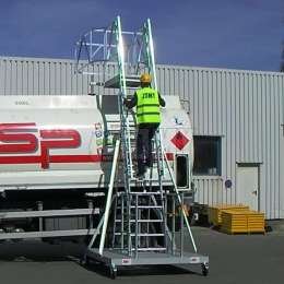 Worker climbing on a mobile ladder used for accessing tanker truck manholes.