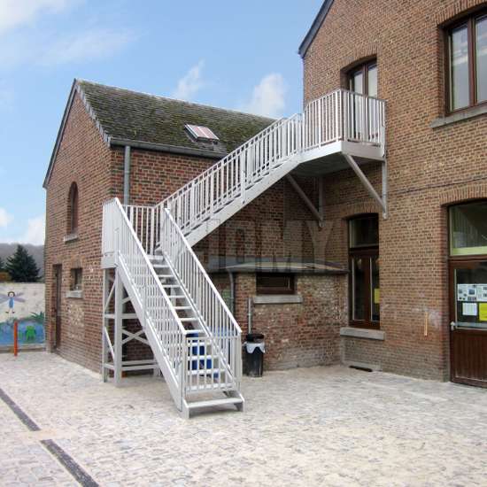 Exterior metal stairs with landing used to access the 1st story of a brick school.