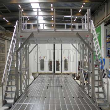 Plataforma de trabajo industrial con escaleras de acceso y trampilla extraíble en la línea de producción de una fábrica de motores.