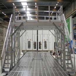 Plataforma industrial en forma de puente con escaleras en aluminio, utilizada en una línea de producción de motores.