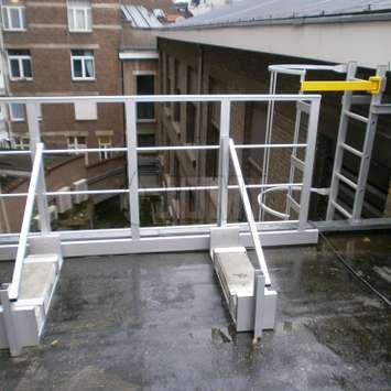 Safety guardrail with ballast for accessing a cage ladder on a roof.