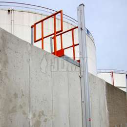 Closed JOMY retractable ladder installed on a facility wall outside of a storage tank area.