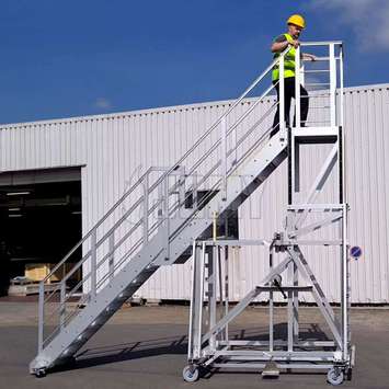 Worker climbing up the stairs of JOMY's height adjustable work platform.