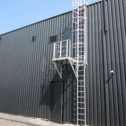 Zugangsbalkon seitlich zu einer Krinoline-Leiter für eine äußere Nottür auf einem Industriegebäude mit Metallverkleidung.